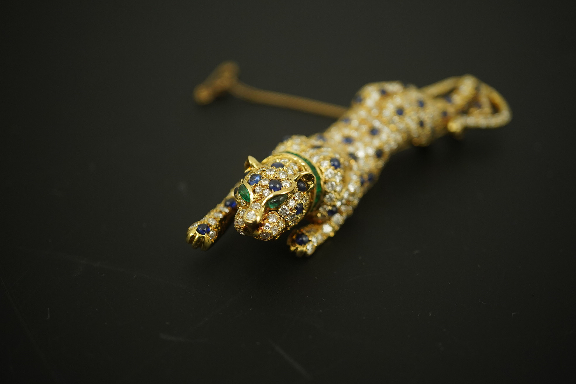 A modern Cartier style 18k gold, sapphire, emerald and diamond cluster set stalking panther brooch